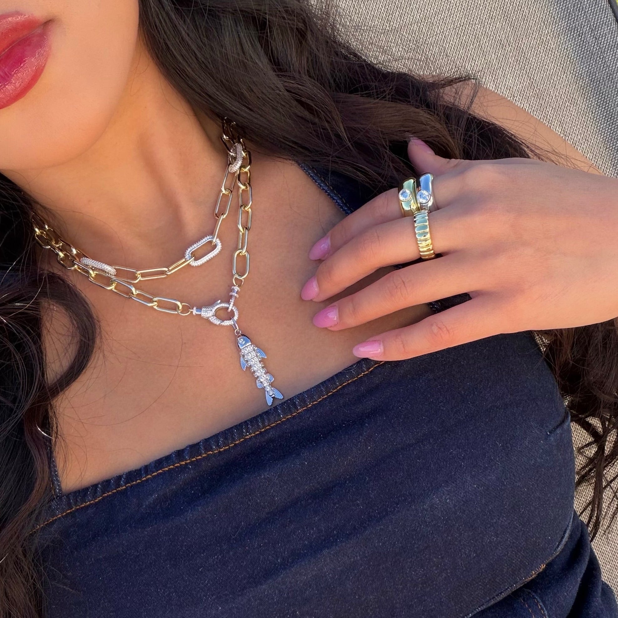 Close-up of a person wearing a gold chain necklace and ring with a blurred background